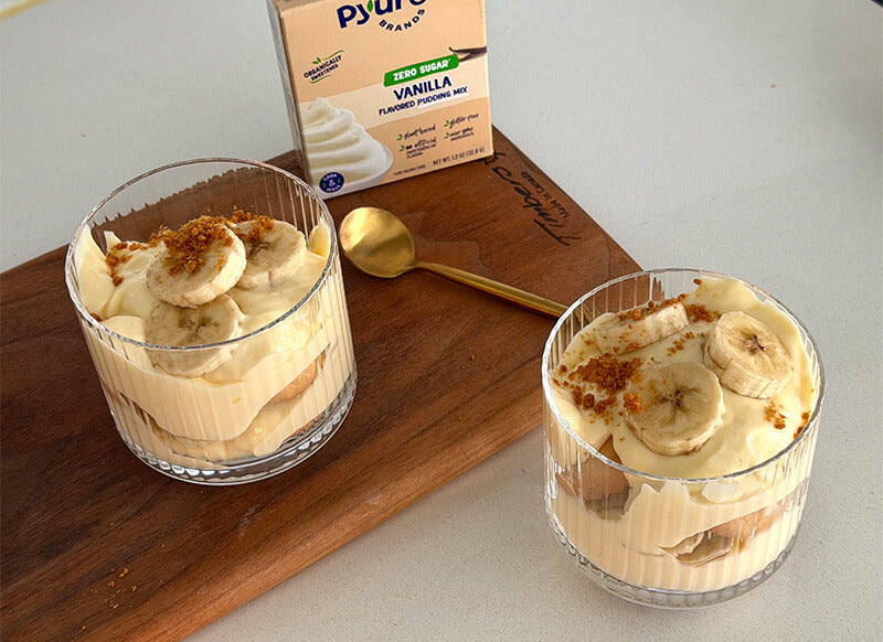Low-Sugar Banana Pudding in glass cups with spoon and Pyure sugar-free vanilla pudding mix box
