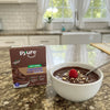 Pyure chocolate pudding mix box with a bowl of pudding on a kitchen counter